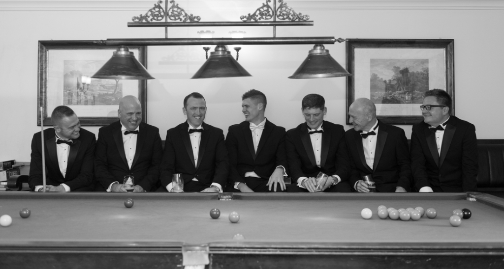 Groom and his groomsmen laughing together while playing snooker