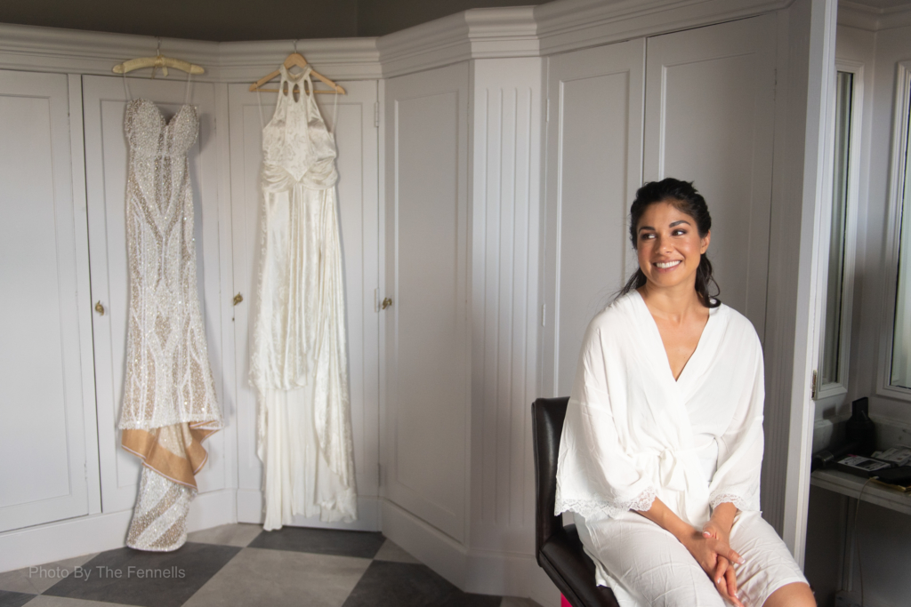 Sarah Roberts sitting on a chair in her wedding robe in front of her two wedding dresses
