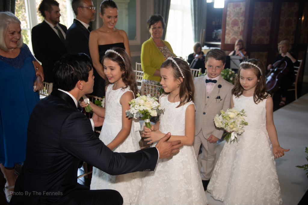 The flower girls and pageboy walking up the aisle being greeted by the groom