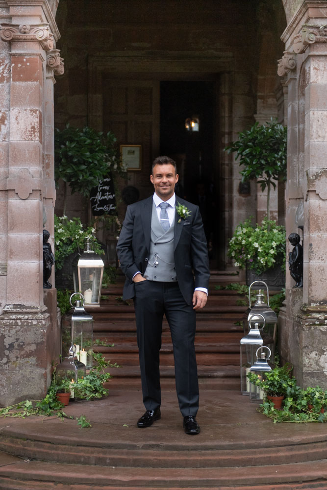 Groom in suit standing on front steps of Castle Leslie Estate