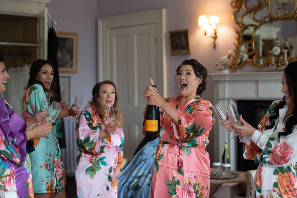 Bridesmaid popping champagne with Bridal party