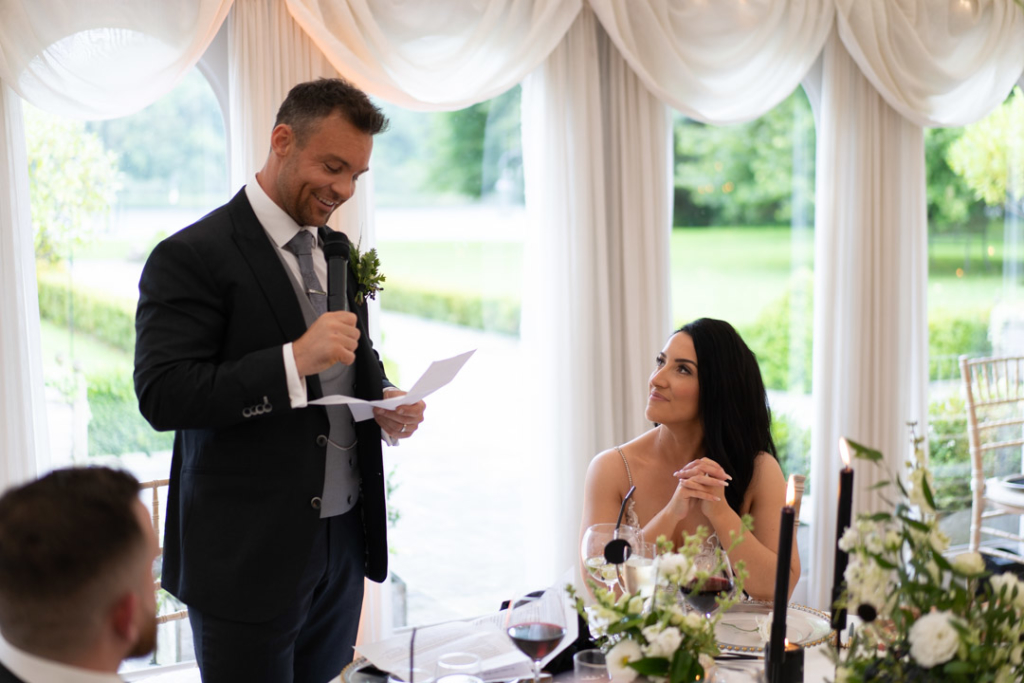 Groom standing giving speech while the Bride is looking at him