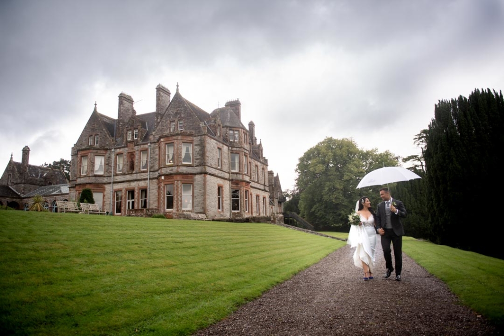Bride and groom walking under umbrella at their castle leslie wedding in Ireland