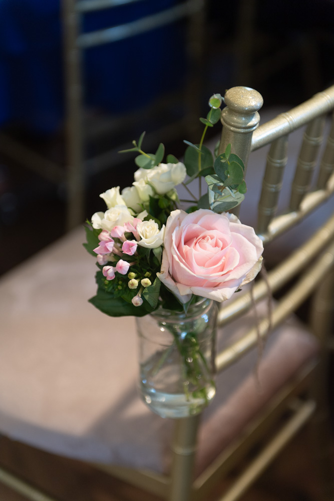 Pink flower in a glass jar hanging on the side of chair for wedding ceremony