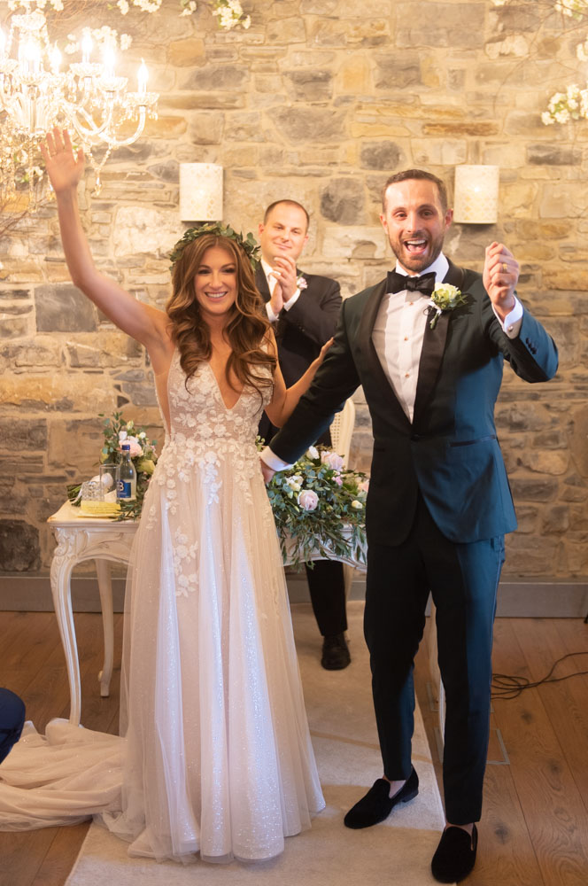 Bride and groom cheering with hands in the air after being announced as just married