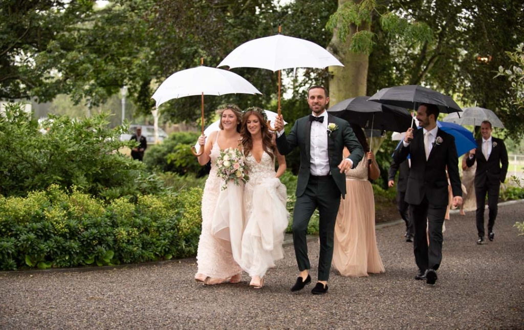 Bridal party walking in the rain with umbrellas at Ballymagarvey village