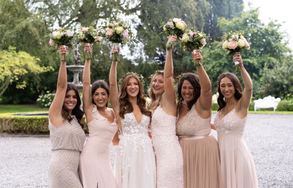 Bride and Bridesmaids laughing with their flowers held over their heads