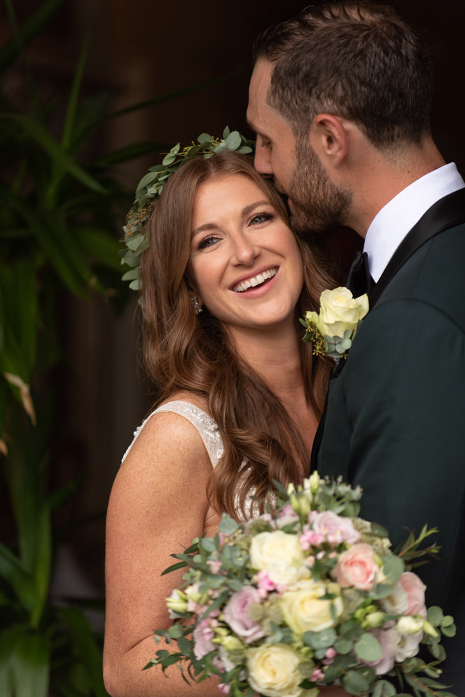 Bride laughing while groom kisses the side of her face