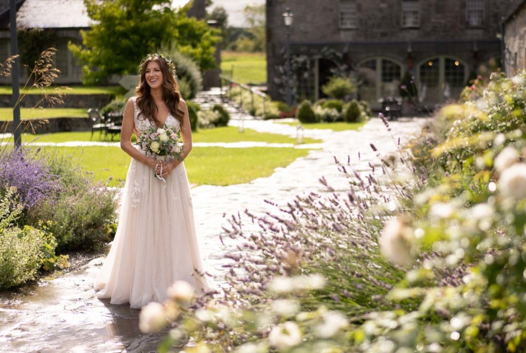 Bride standing in the courtyard at Ballymagarvey village surrounded by summer flowers