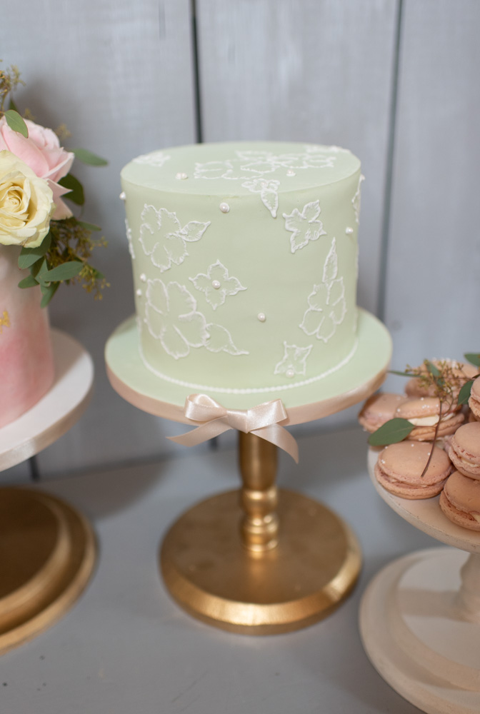 Green one tier wedding cake with white pearls and decoration sitting  on a gold cake stand