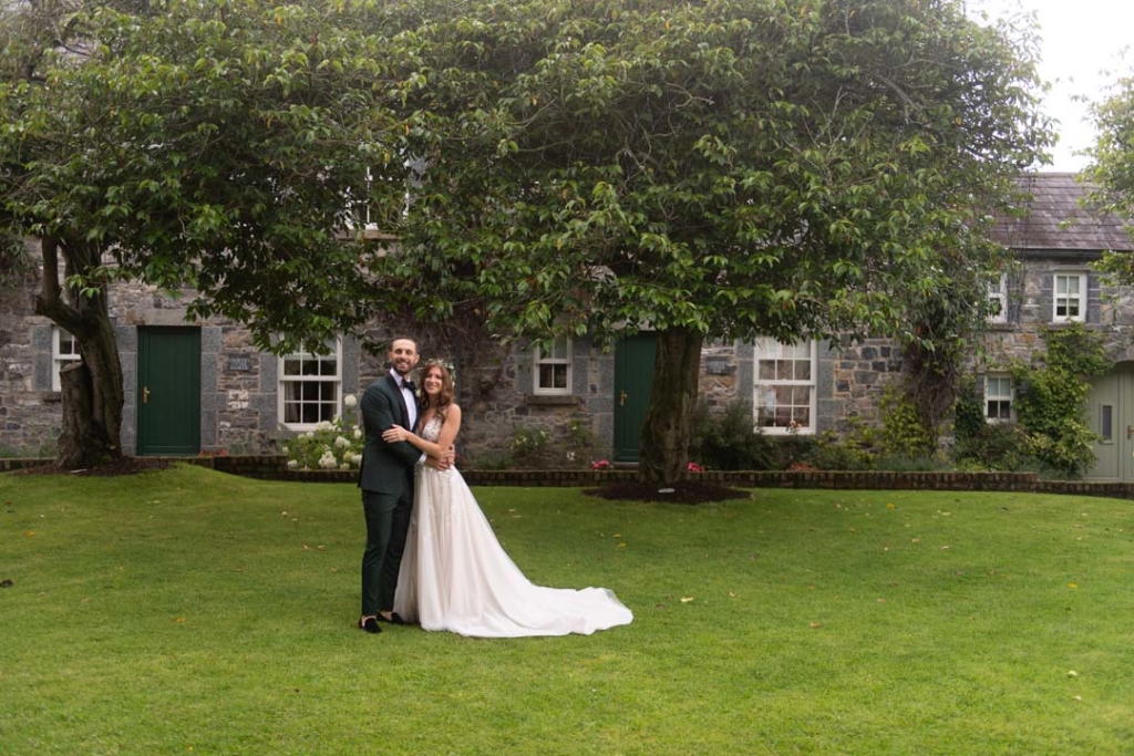 Bride and Groom standing on grass arm in arm smiling at camera in the courtyard of Ballymagarvey 