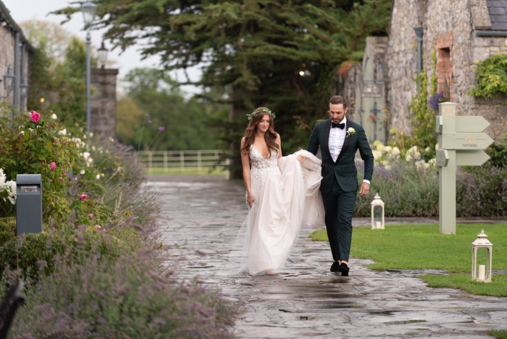 Groom holding up Brides dress as they walk through Ballymagarvey