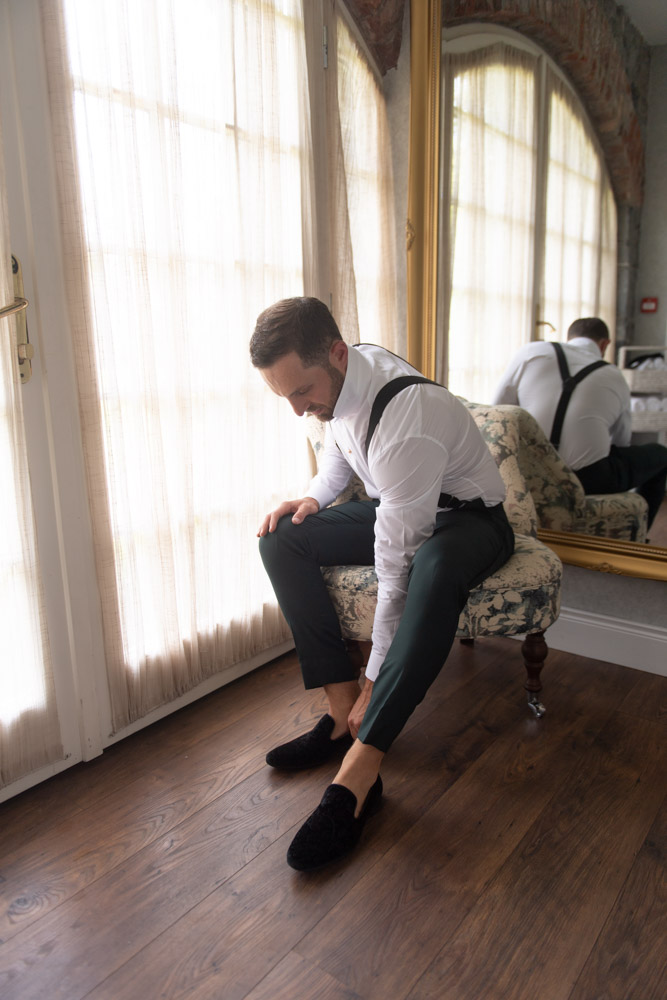 Groom seated putting on his black velvet slip on shoes