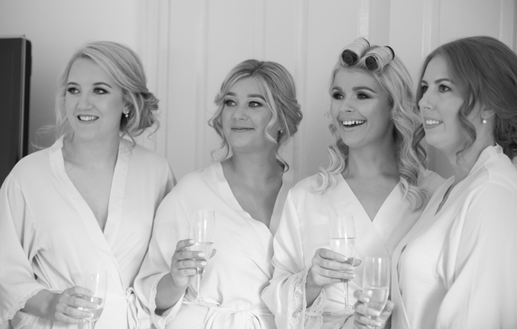 Bride and bridesmaids in white robes holding champagne glasses