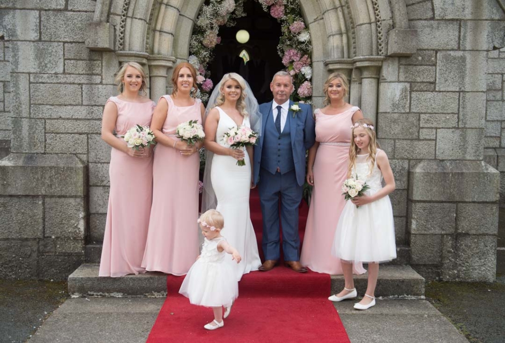 Bride and her dad and bridesmaids standing in front of church doors