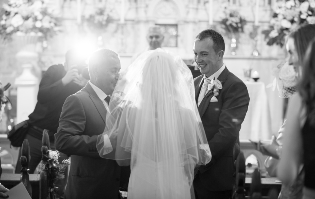 Groom smiling and greeting the bride and her dad at the top of the aisle