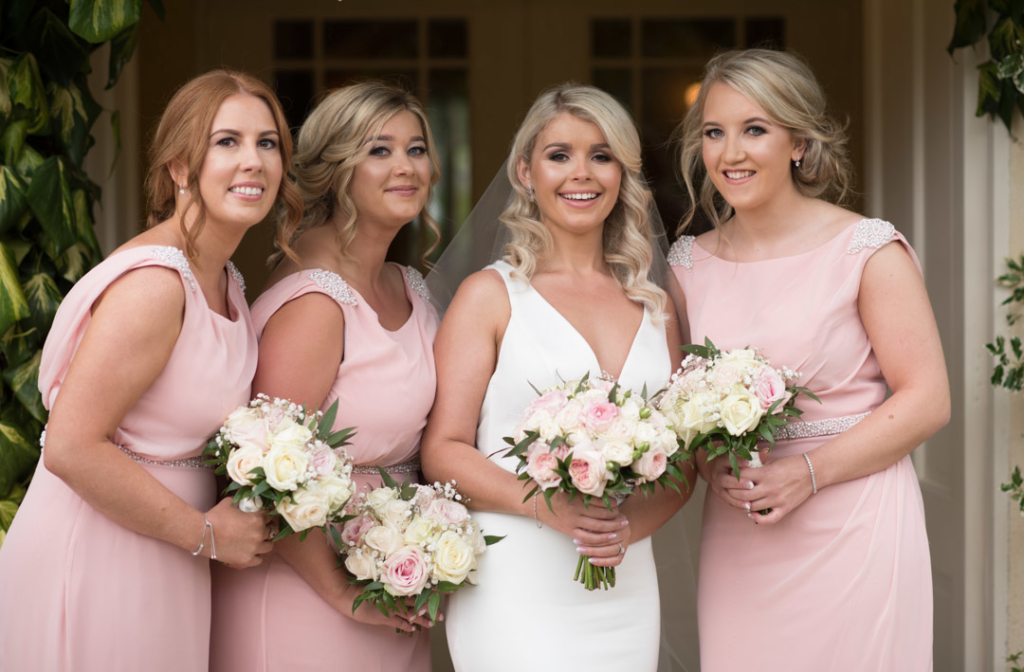 Bride and bridesmaids standing together while holding pink and white flower bouquets