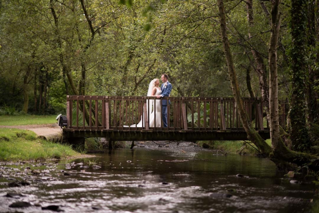 Bride and groom standing on wooden bridge over the river in Brooklodge