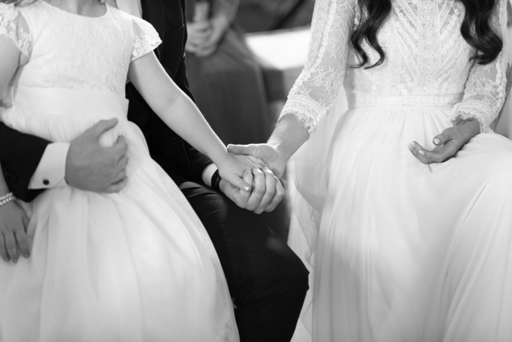 Bride and groom and their daughter holding hands together