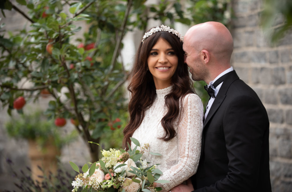 Bride and groom smiling and embracing in front of apple tree at the Mill House Slane
