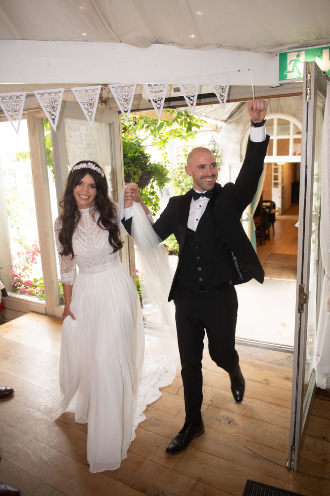 Bride and groom walking into their dinner reception room with their guests cheering
