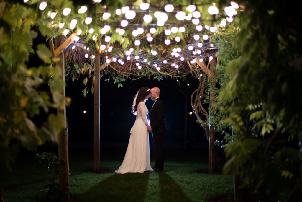 Bride and groom outside at night embracing under the fairy lights