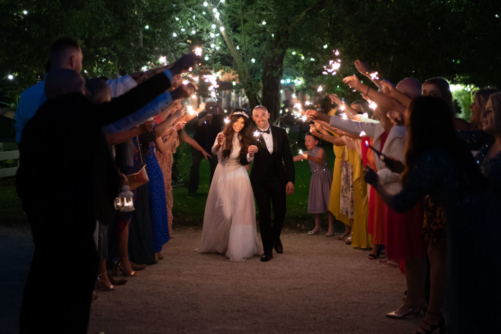 Bride and groom walking through a tunnel of sparklers that their guests are holding