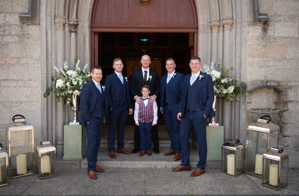 The groom and his groomsmen and pageboy standing in front of the Church doors