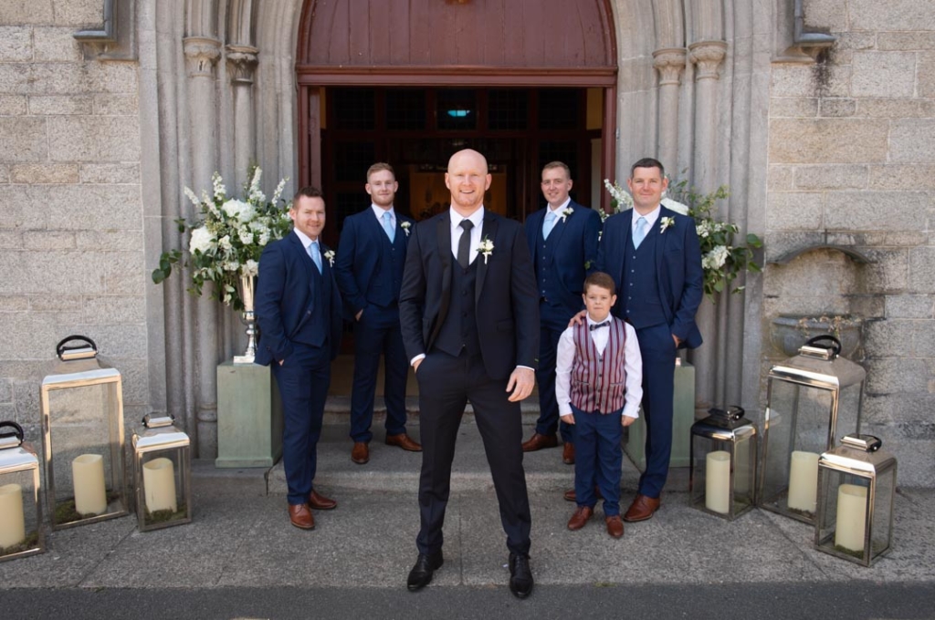 The groom standing in front of the Church with the groomsmen and pageboy in the background