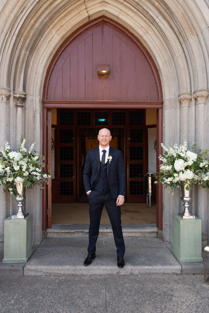 Groom standing in the Church door with flowers in silver vases either side of the door