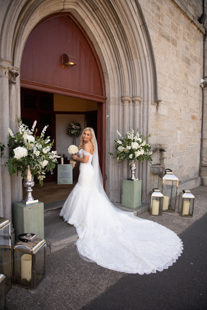 Bride holding her wedding bouquet and looking back over her shoulder at camera outside the church doors