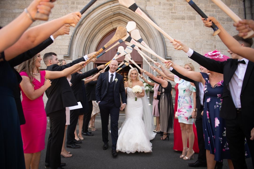 Bride and Groom walking under a hurley stick archway that their friends are holding