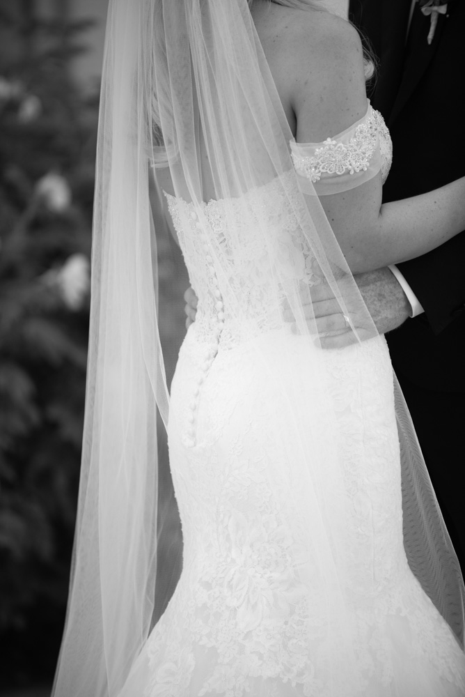Black and white close up of Brides dress and the Grooms hands on her waist
