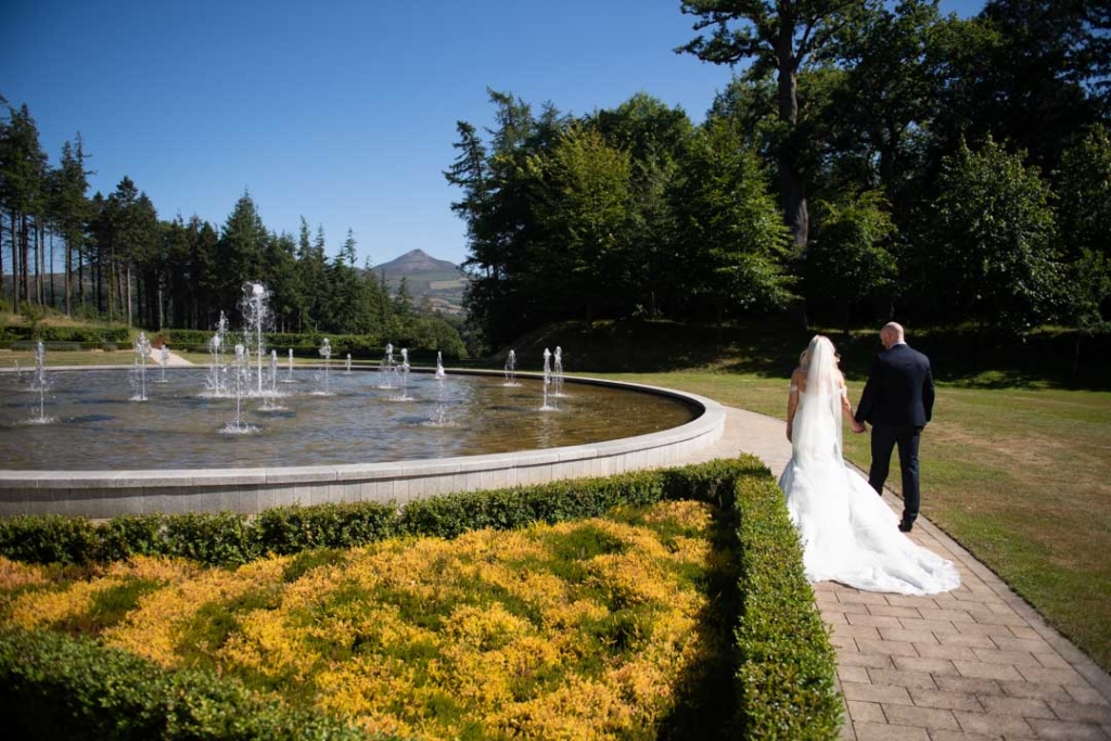 Bride and Groom walking holding hands beside water fountain and the sugar loaf mountain behind