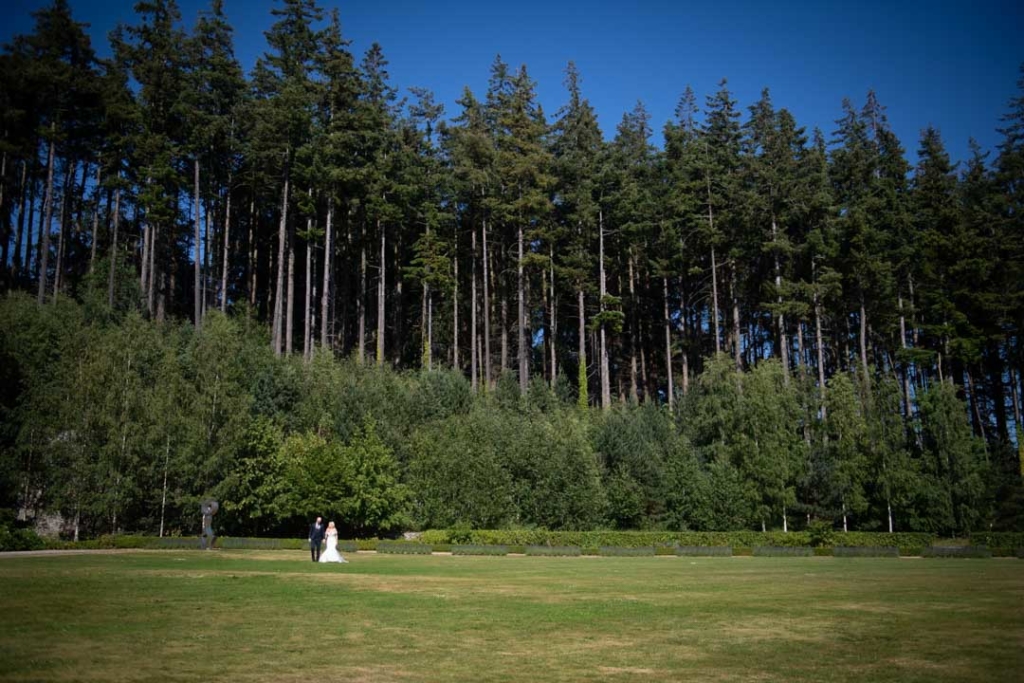 Bride and Groom walking in front of tall trees on the grounds of Powerscourt Hotel