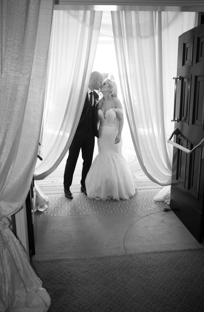 Black and white of Bride and groom kissing at the doorway into their dinner reception