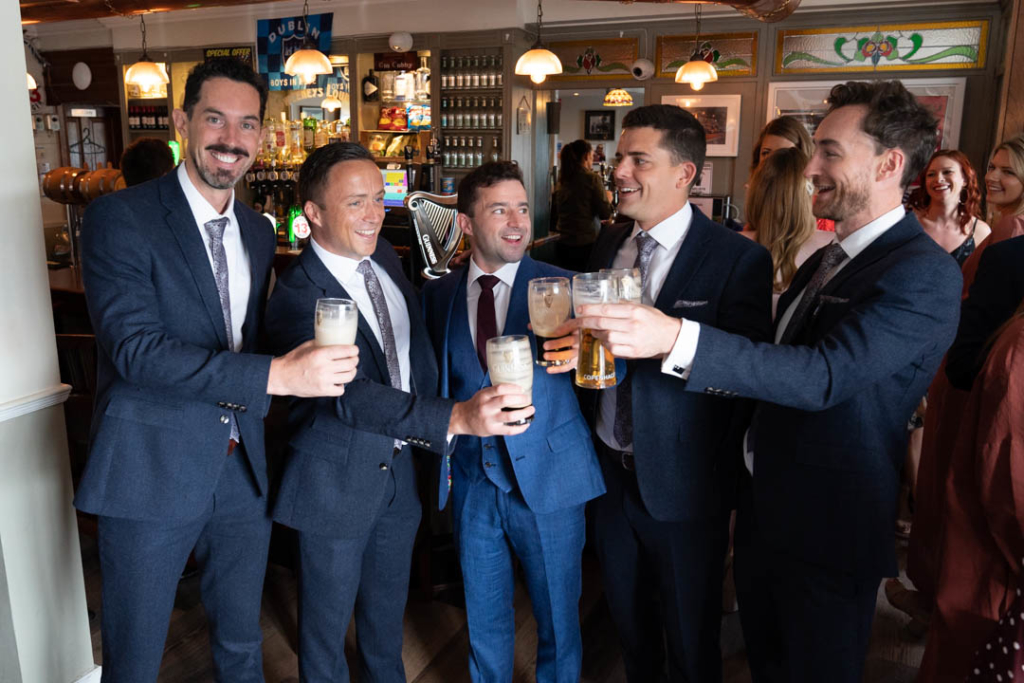 Groom and groomsmen in the pub clinking pint glasses