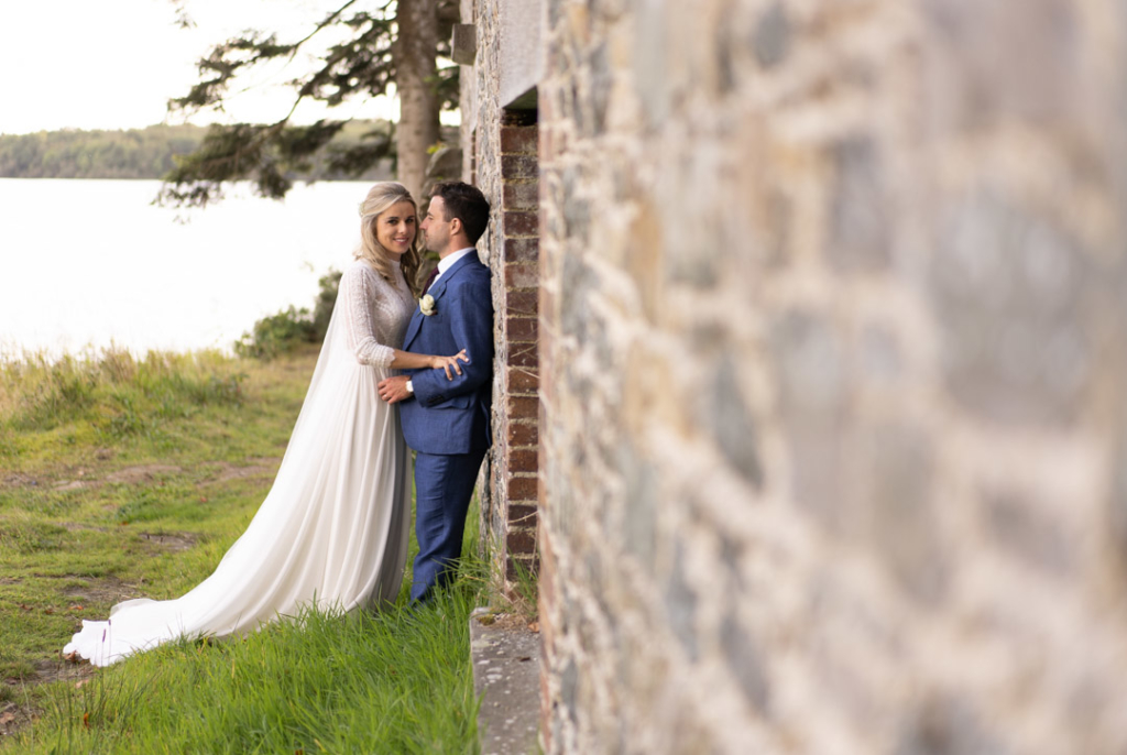 Bride and groom leaning against boathouse wall arm in arm