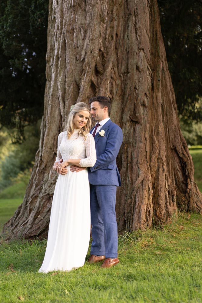 Bride and groom embracing by a big oak tree on the grounds of Virginia Park Lodge
