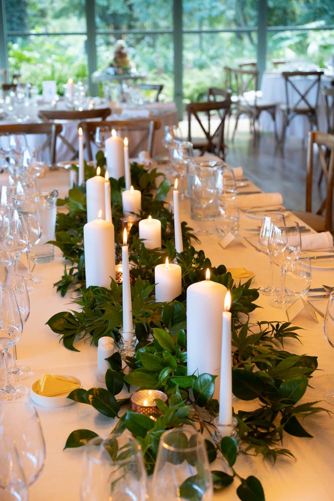 The top table centre piece with greenery and white pillar candles